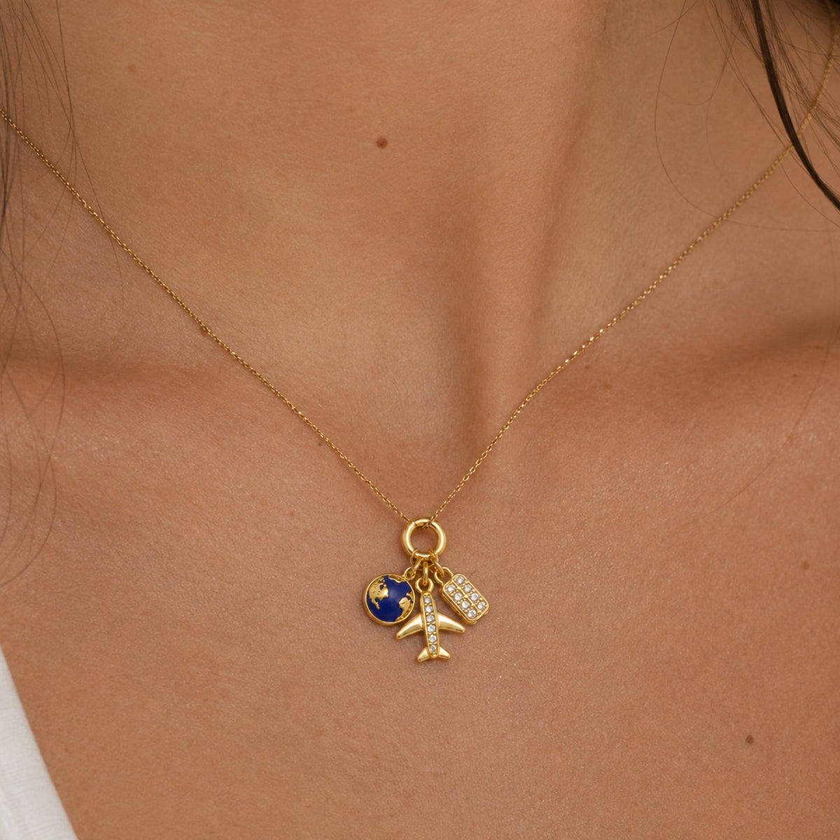 Charm de viajes colgado de una cadena, puesto al cuello, en otro plano