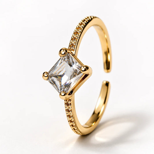 Anillo dorado ajustable con una piedra rectangular transparente y banda en pave