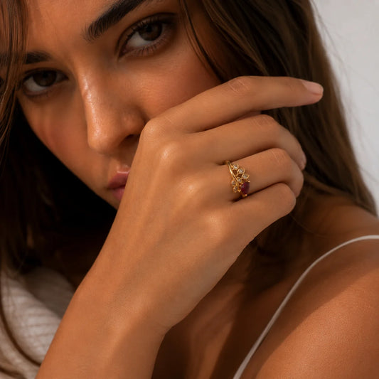 Mujer con la mano en el rostro y el anillo de hoja con piedra roja