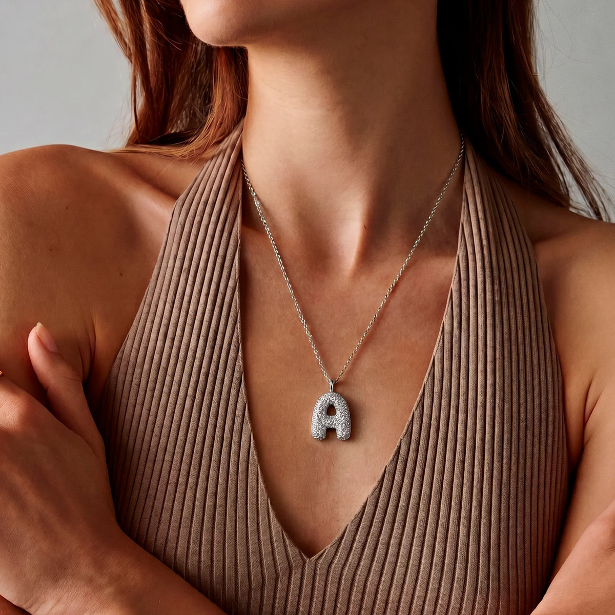 Collar de inicial bubble en plata puesto, la cadena cae debajo de la clavícula