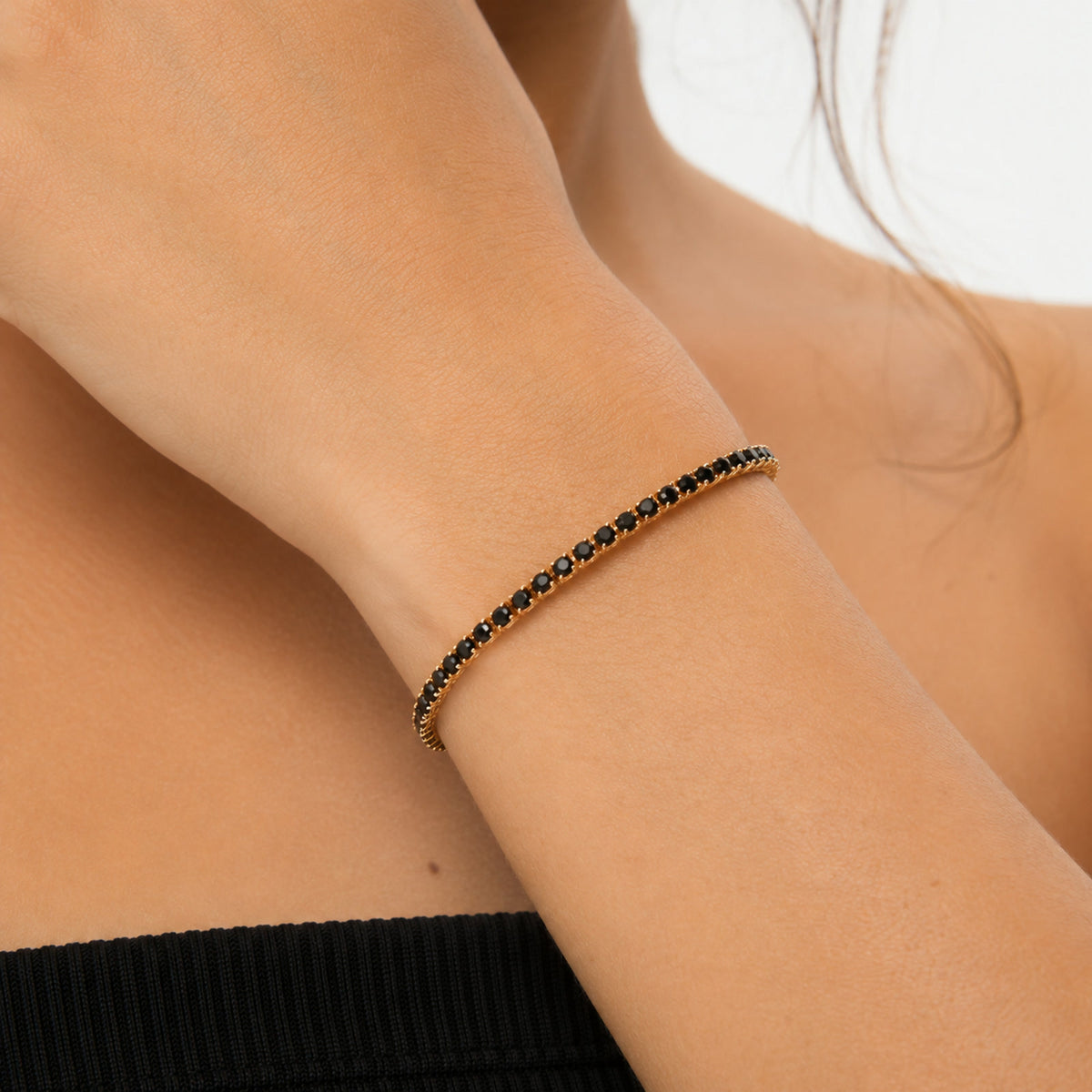 Pulsera tenis de piedras negras puesta en la muñeca, en otro plano